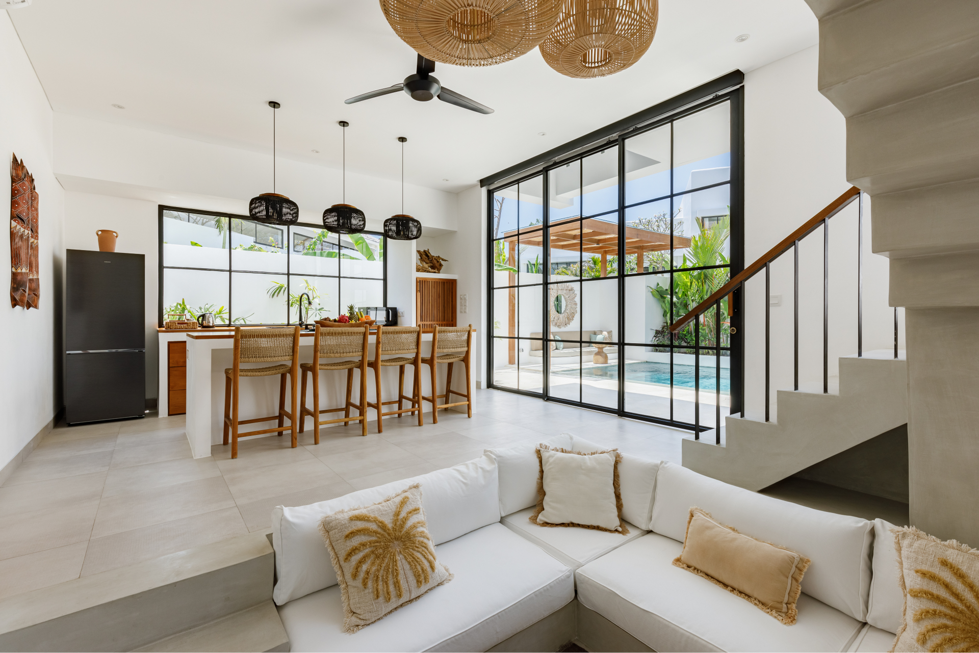 Bright open-plan living room with white sofa, wooden dining table, black-framed windows, and staircase