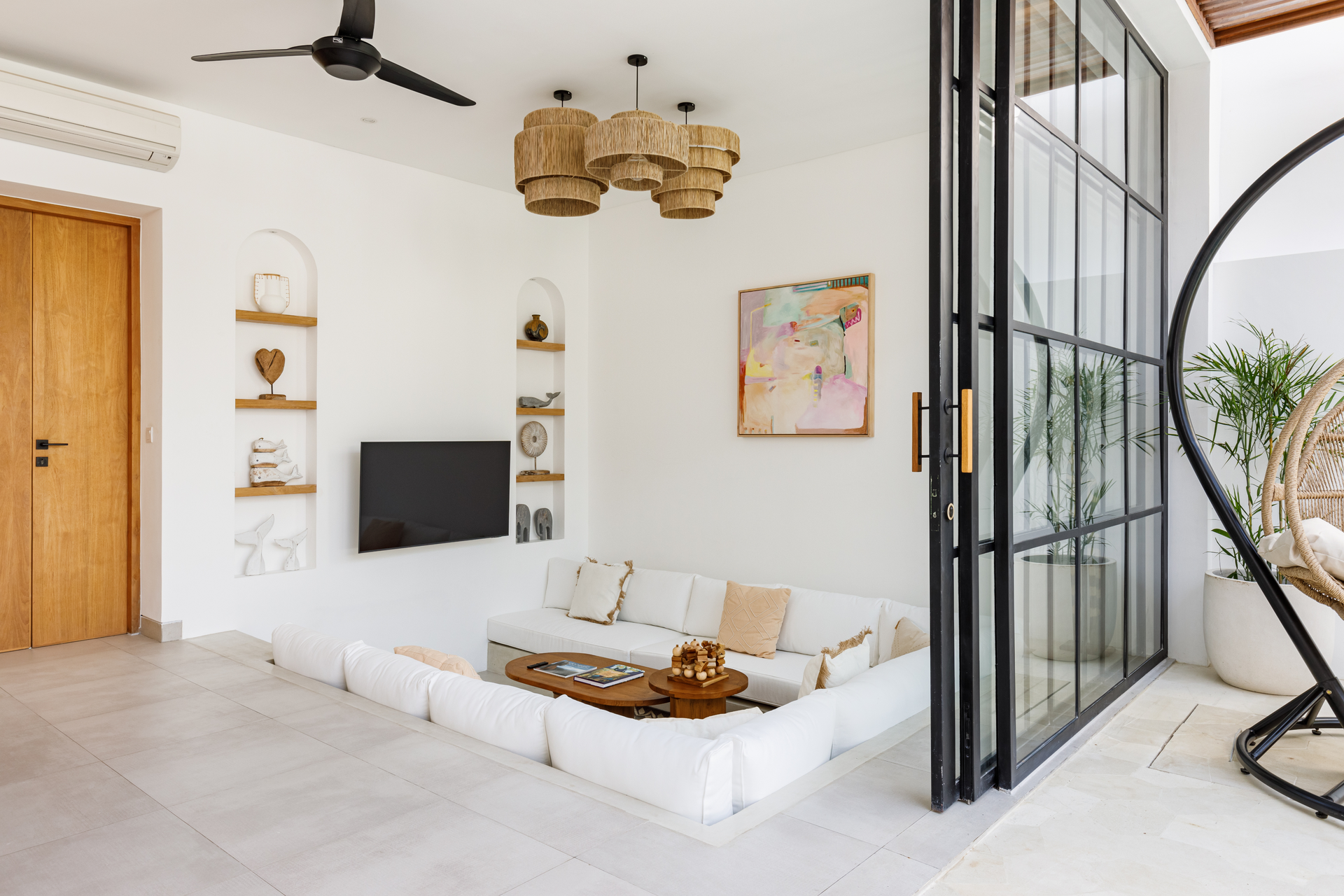 Bright minimalist living room with a white sofa, wall-mounted TV, ceiling fan, and open glass doors.