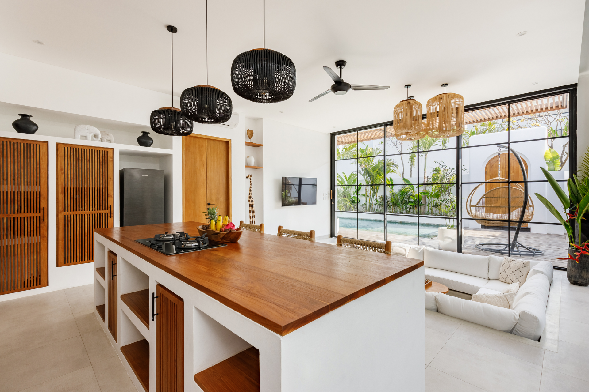 Bright modern kitchen with wooden island, white seating area, and large windows overlooking greenery