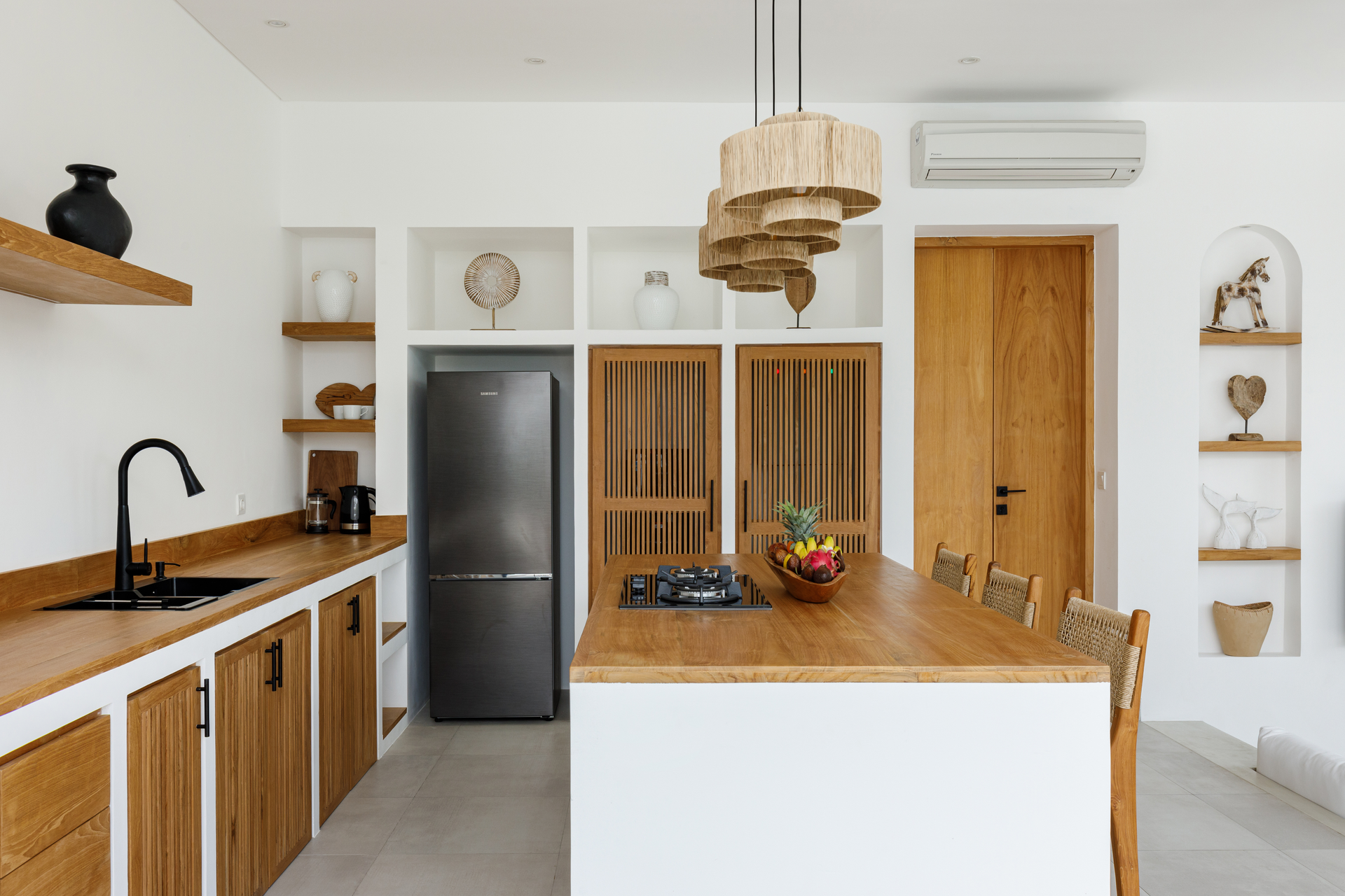 Modern kitchen with wood cabinets, white island, black faucet, stainless fridge, and woven pendant lights