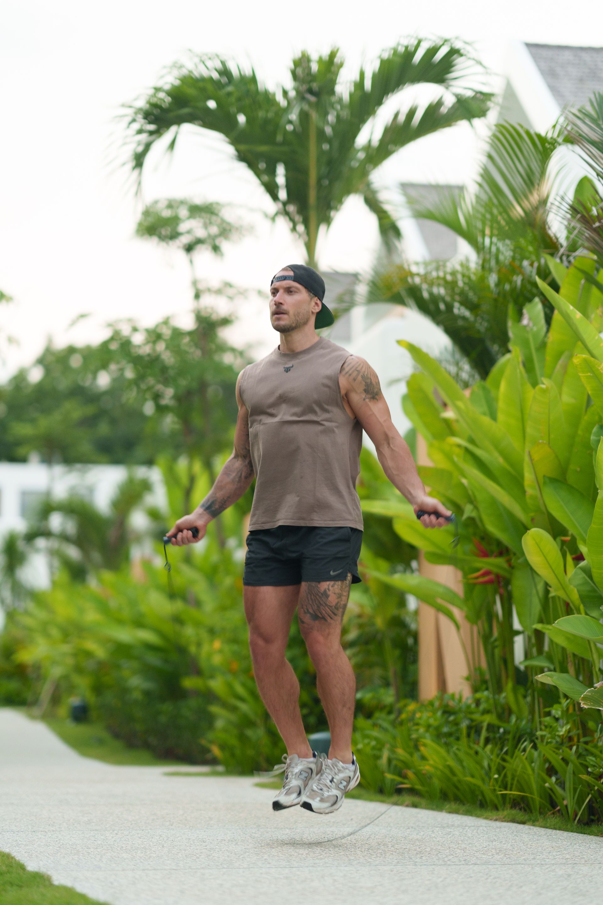 Man skipping rope on a path in a lush tropical garden, surrounded by green plants.