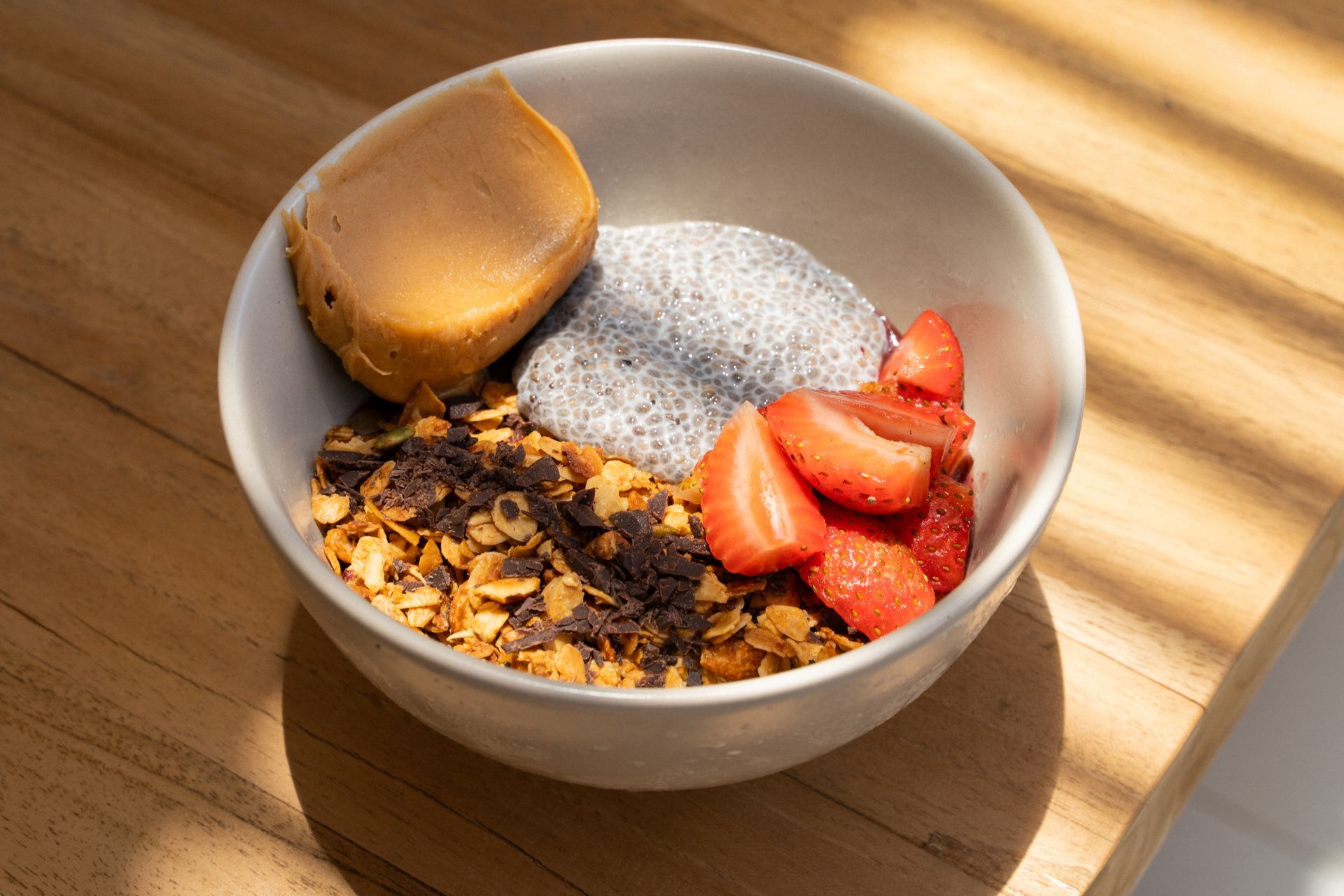 A bowl of granola topped with peanut butter, powdered sugar, and sliced strawberries on a sunlit table