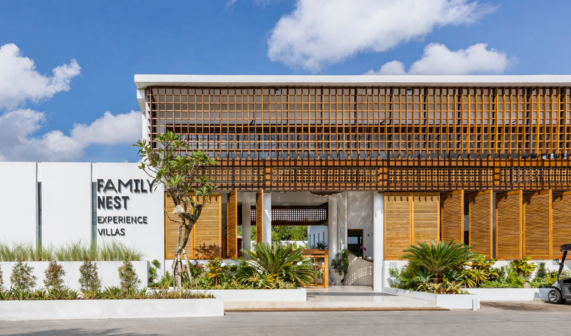 Modern family nest building with bamboo facade, white sign, and landscaped entrance under a blue sky