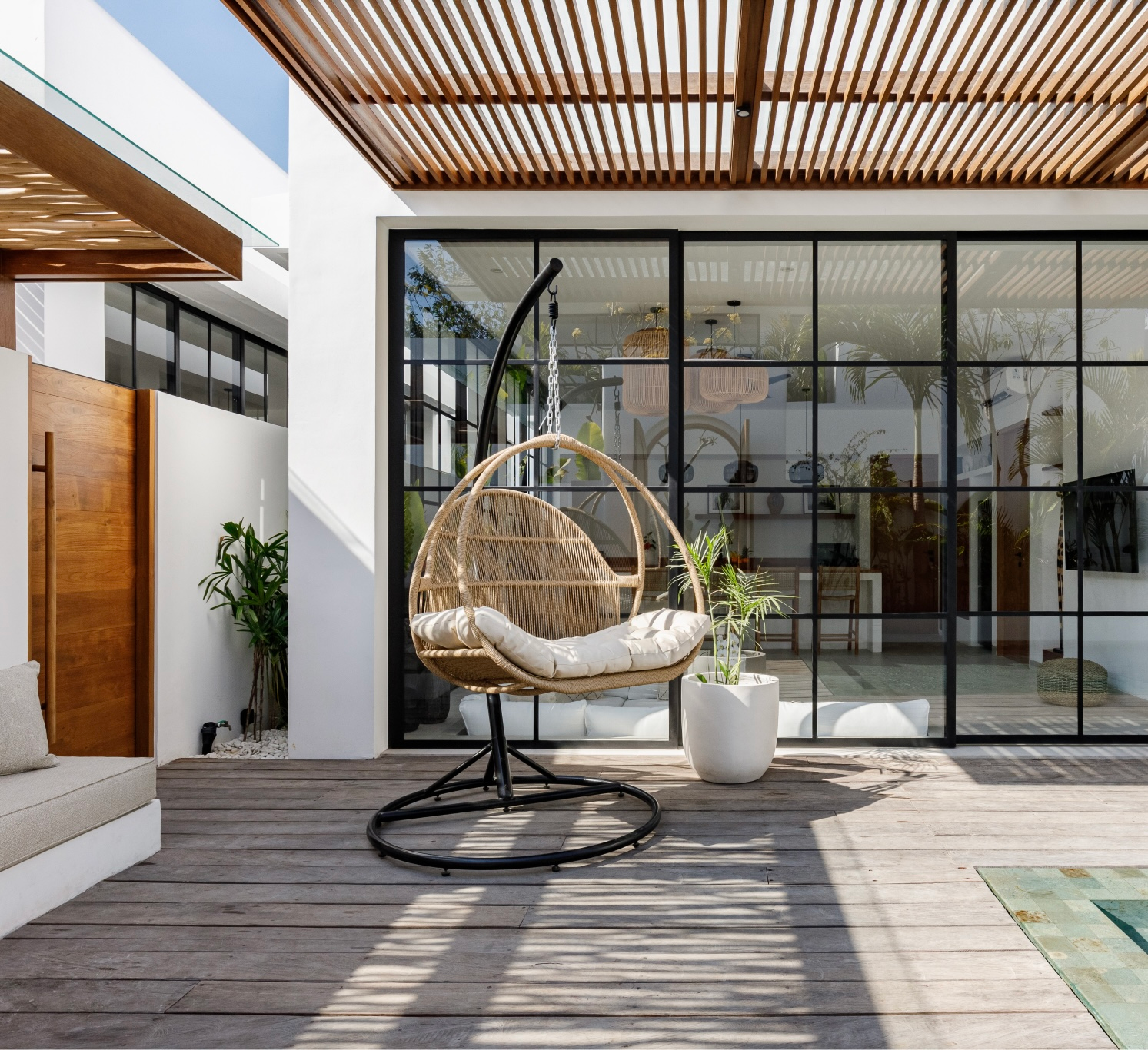 Modern patio with a hanging rattan chair, potted plant, and glass sliding doors under a slatted pergola