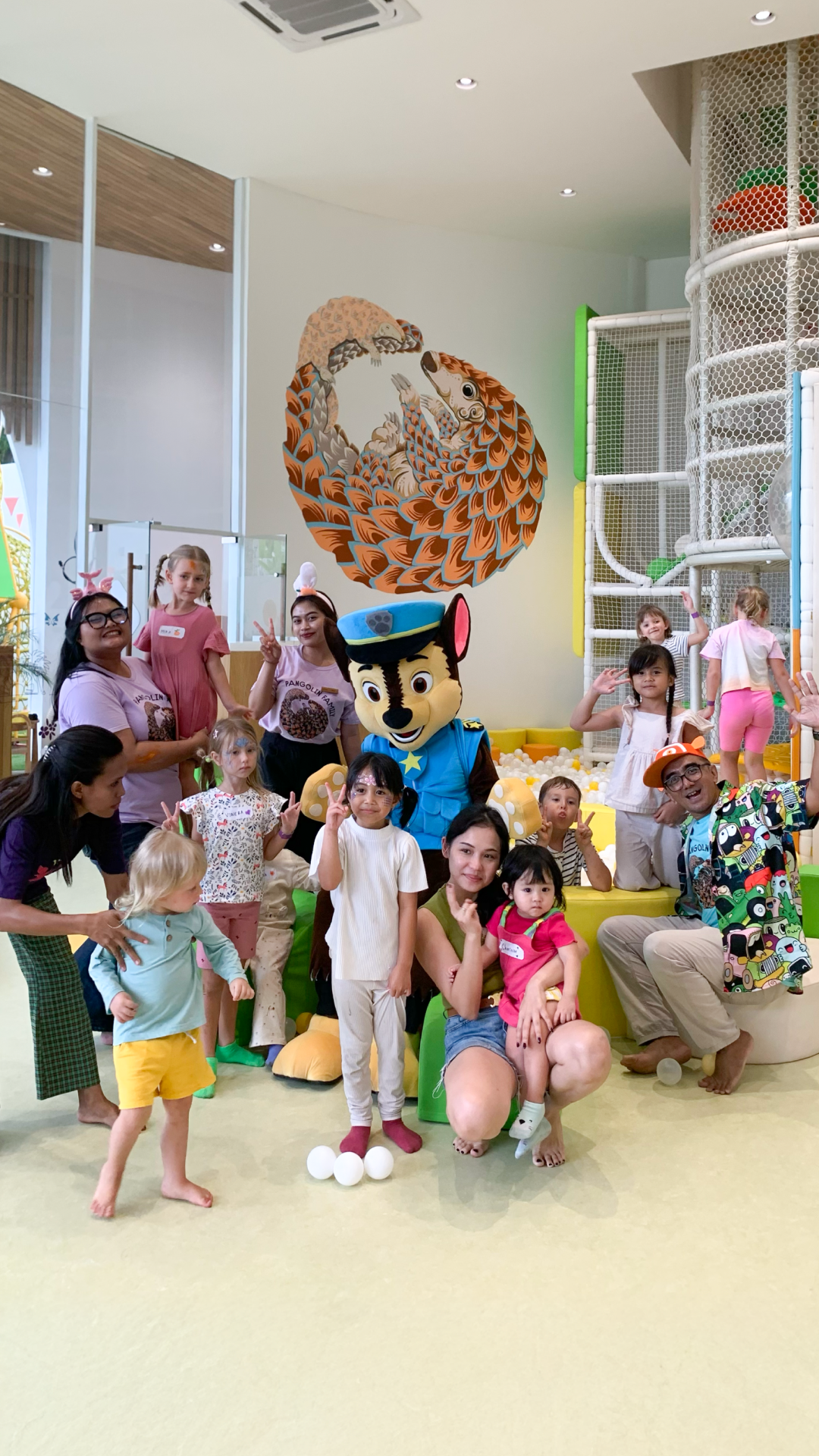 Group posing with a costumed mascot in a bright indoor room with colorful wall art