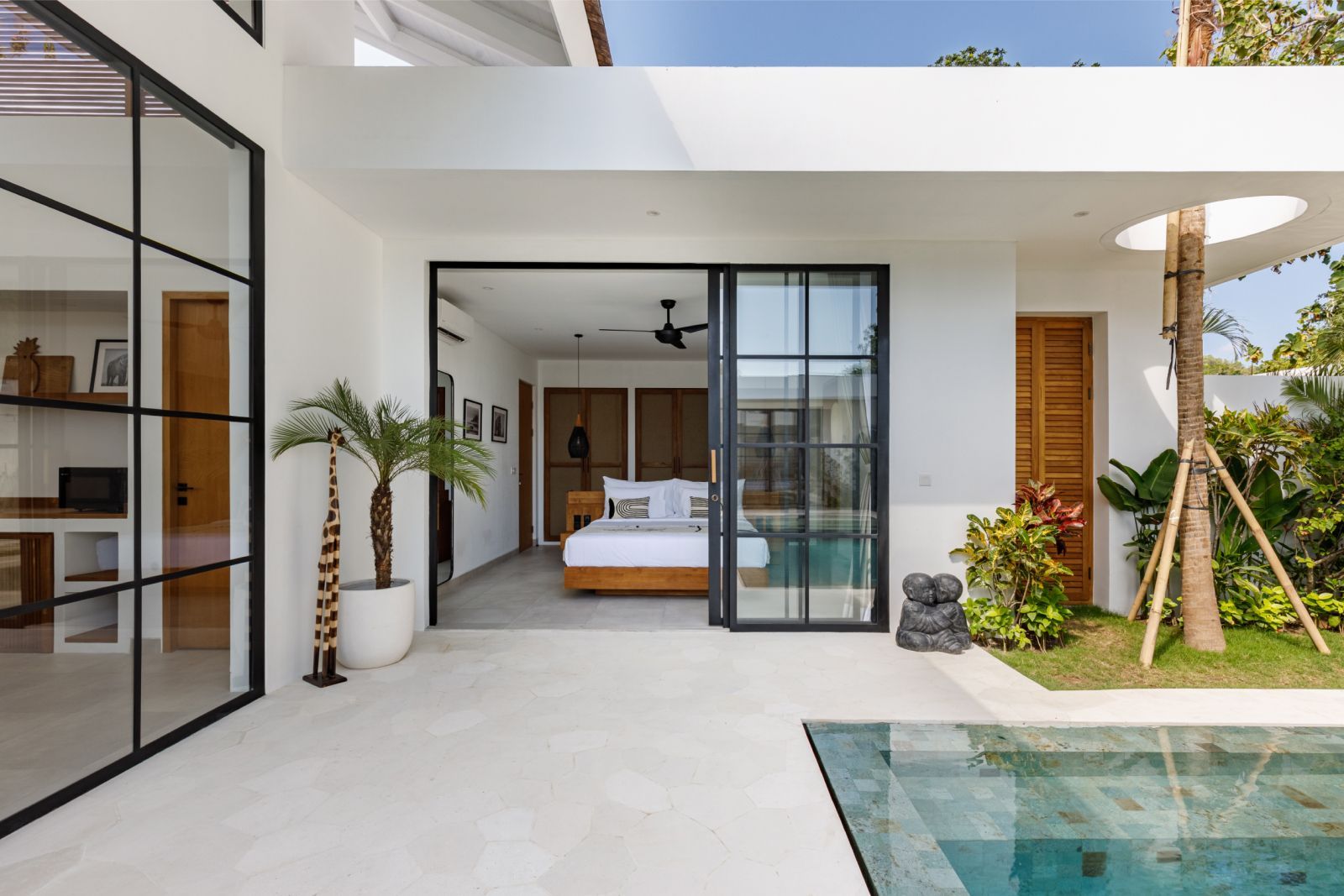 Modern white patio with sliding glass doors, bedroom view, and a small pool beside greenery