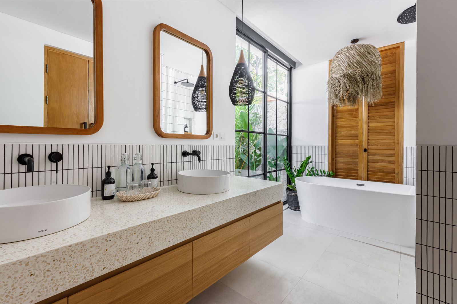 Bright bathroom with double sinks, wood accents, mirrors, a freestanding tub, and a glass shower.
