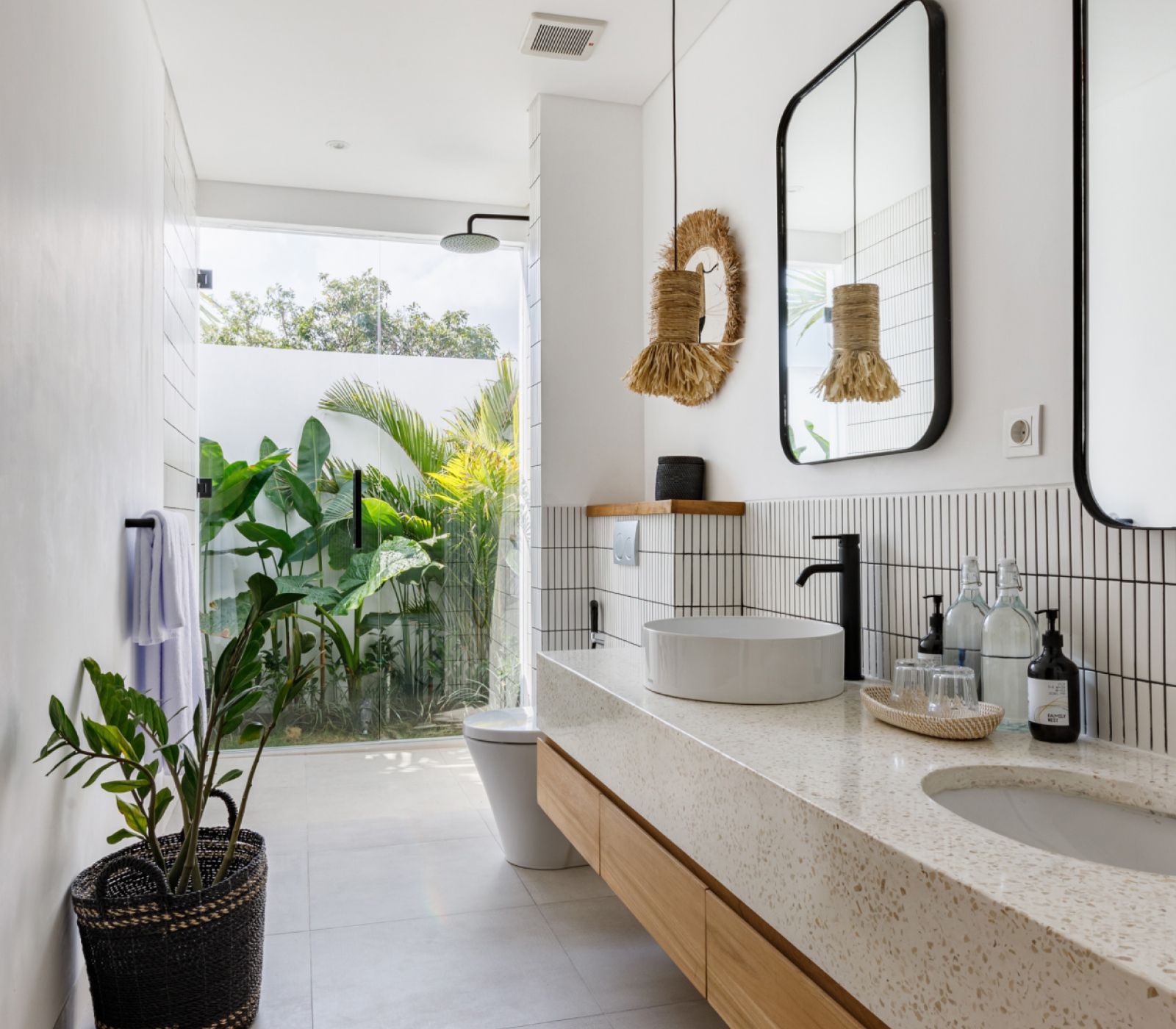 Bright modern bathroom with terrazzo vanity, oval mirror, black fixtures, and potted plants near an open doorway