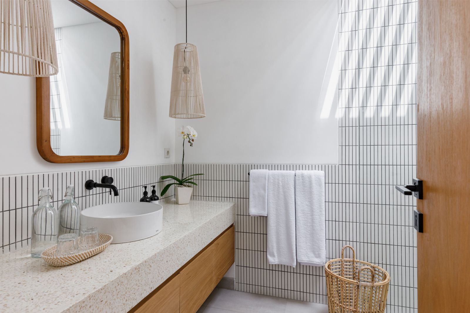 Modern white bathroom with round sink, wood vanity, mirror, striped tile, towel, and wicker basket