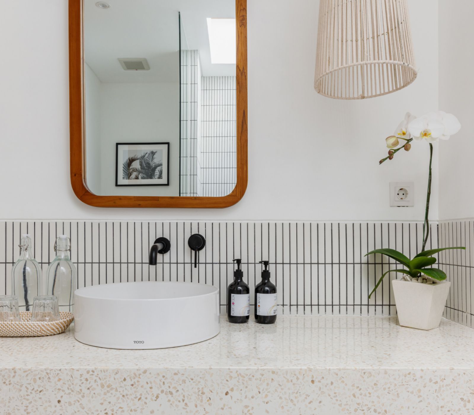 Minimalist bathroom vanity with round white sink, wood-framed mirror, and orchid on a speckled counter
