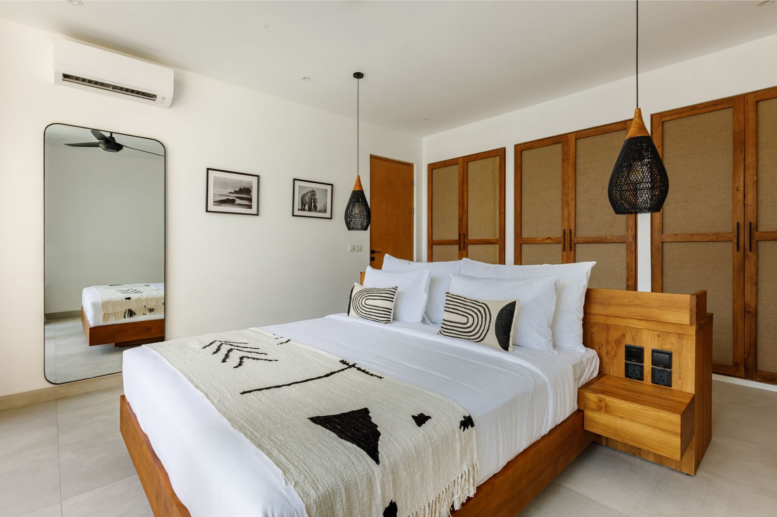 Bright bedroom with a white bed, wooden cabinets, hanging lights, and a full-length mirror.