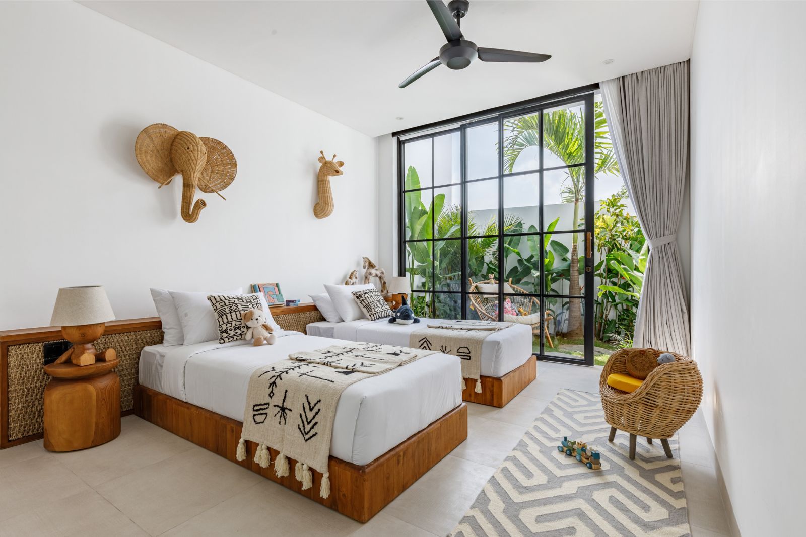 Bright modern bedroom with two beds, woven decor, and large windows overlooking greenery
