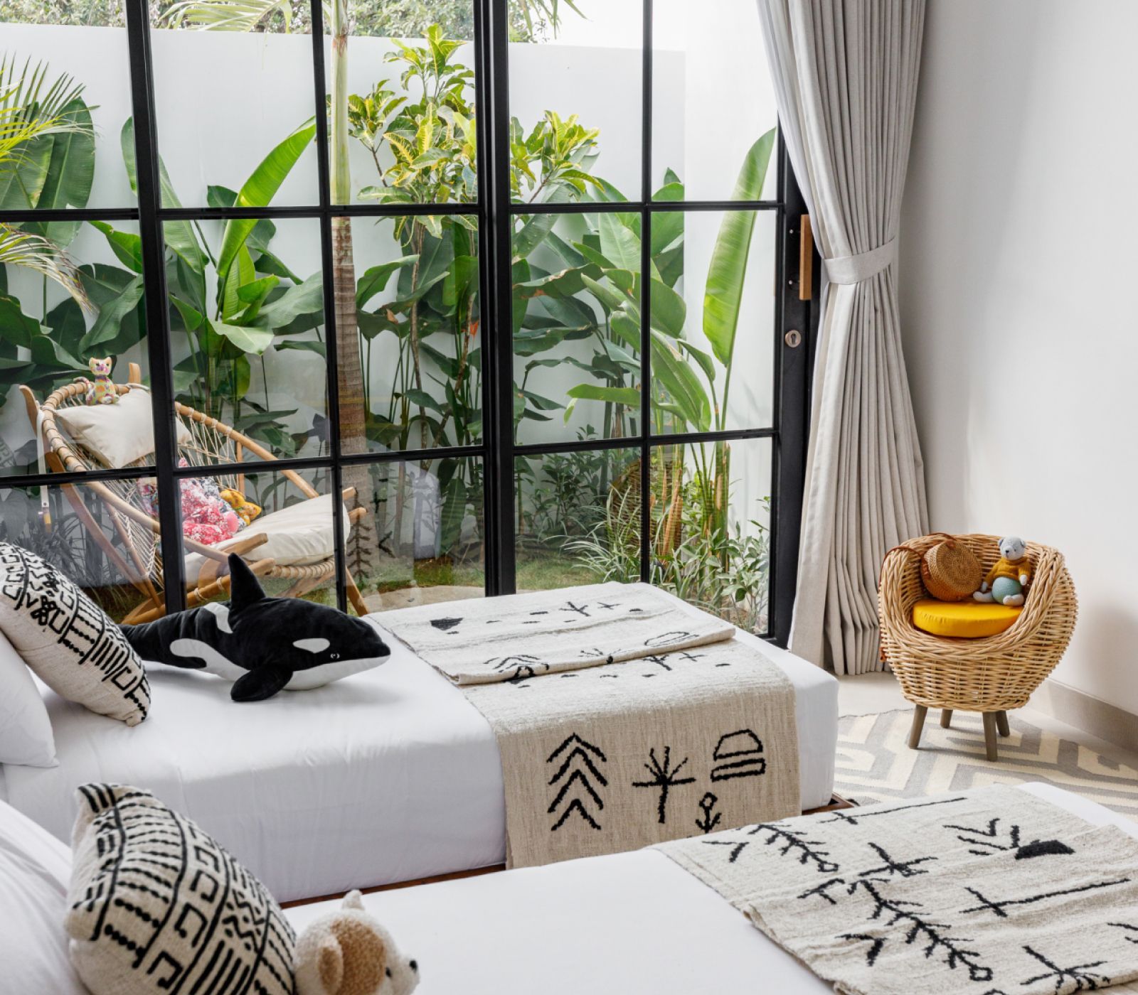Cozy sunlit bedroom with a black cat on a white bed by large windows and a wicker chair