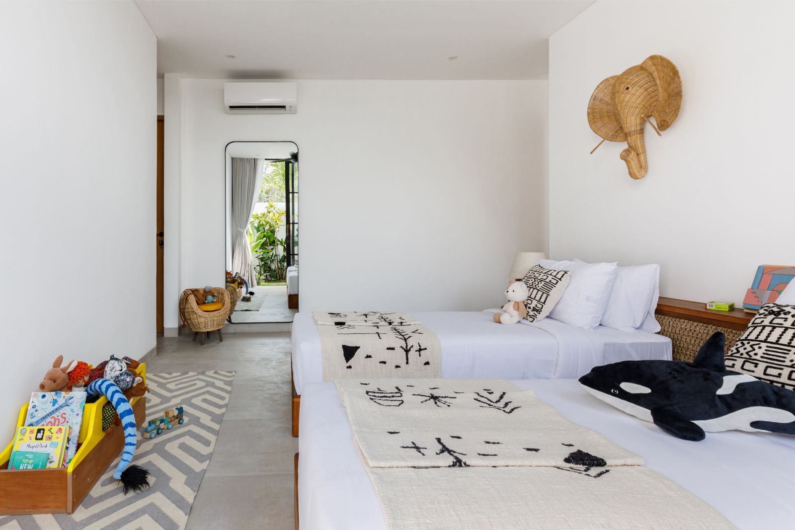 Bright minimalist bedroom with twin beds, white decor, elephant wall art, and toys by a windowed hallway