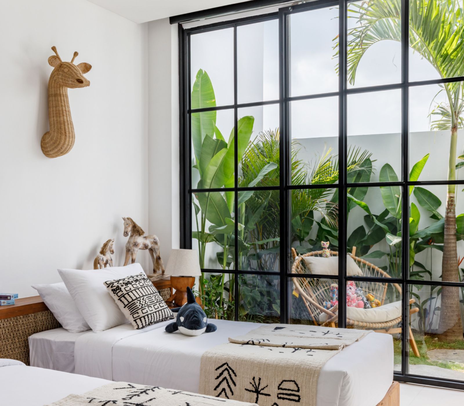 Bright bedroom with a bed by a large black-framed window overlooking lush greenery