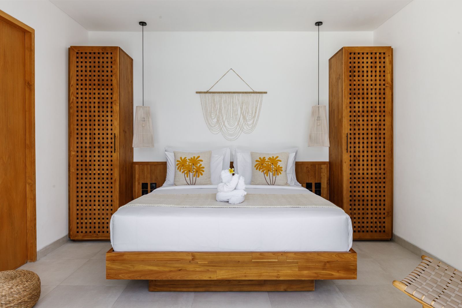 Minimal white bedroom with wooden bed, carved cabinets, and macramé wall decor