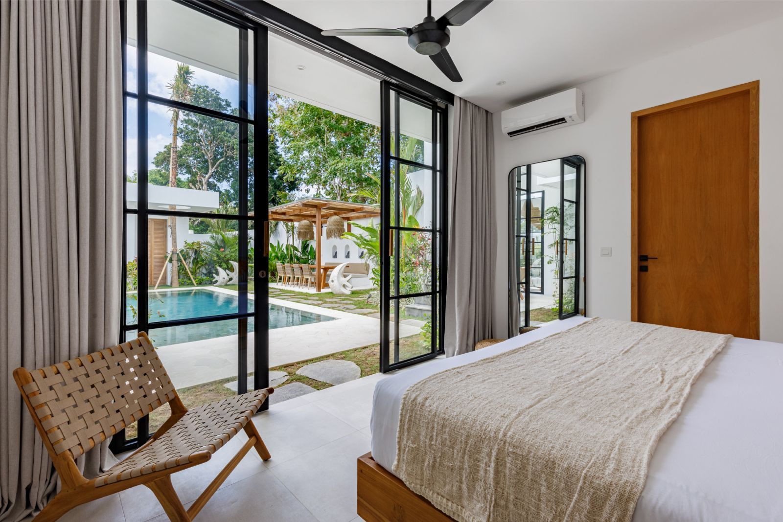 Bright bedroom with large black-framed windows, a view of a pool, and a wooden chair by the bed
