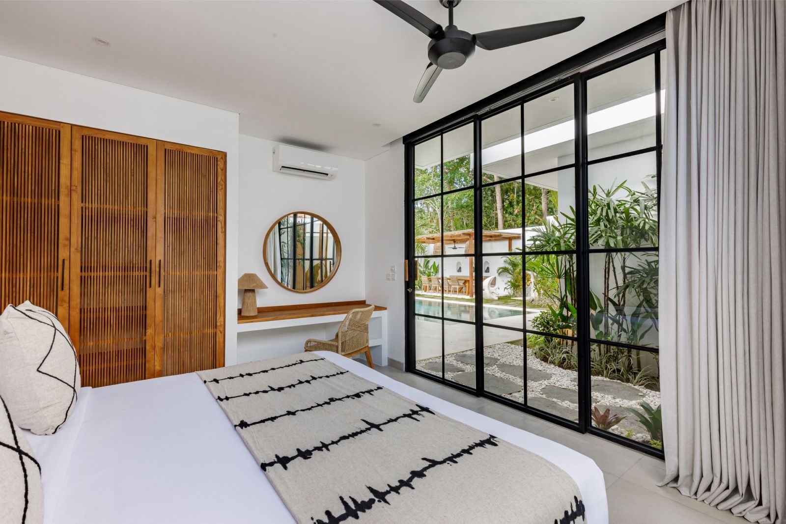 Modern bedroom with king bed, ceiling fan, wood accents, and floor-to-ceiling glass doors to a patio