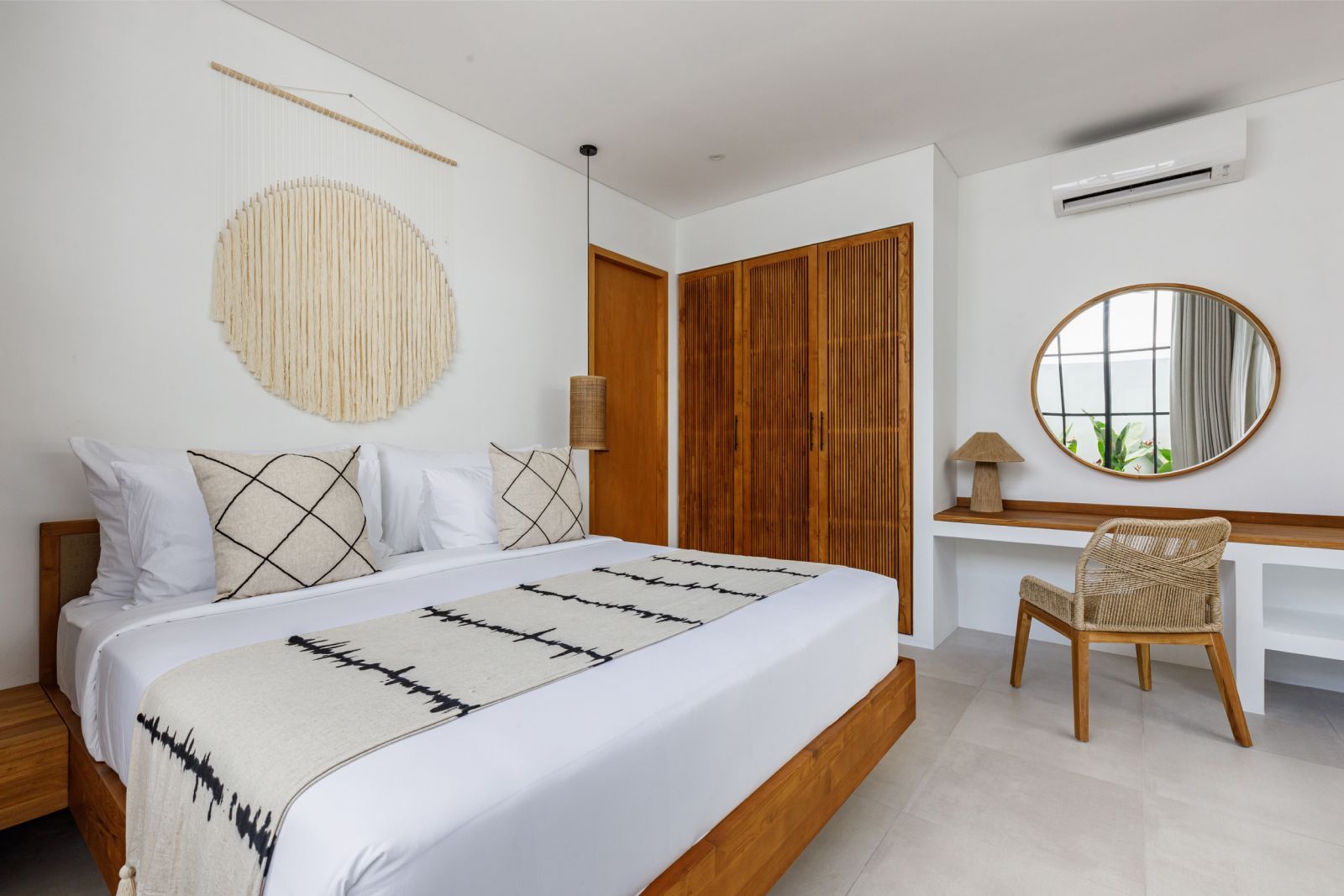 Bright modern bedroom with a wooden bed, white bedding, woven wall decor, desk, and chair