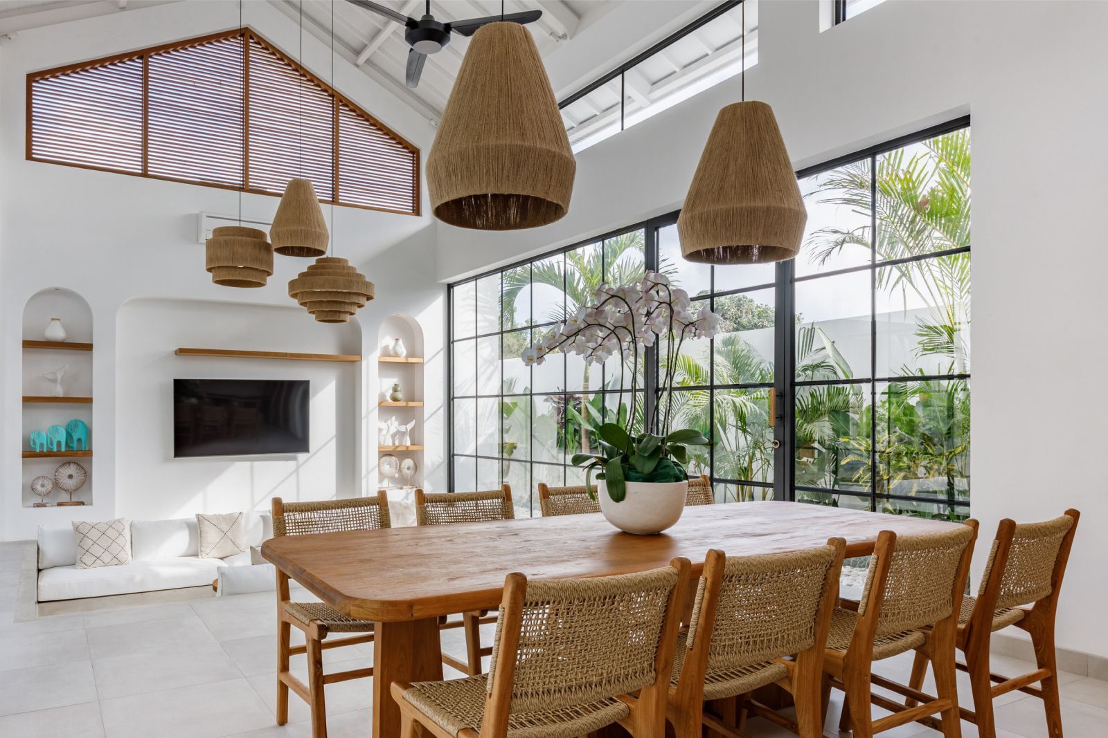 Bright white dining room with rattan table, woven pendant lights, large windows, and indoor plants