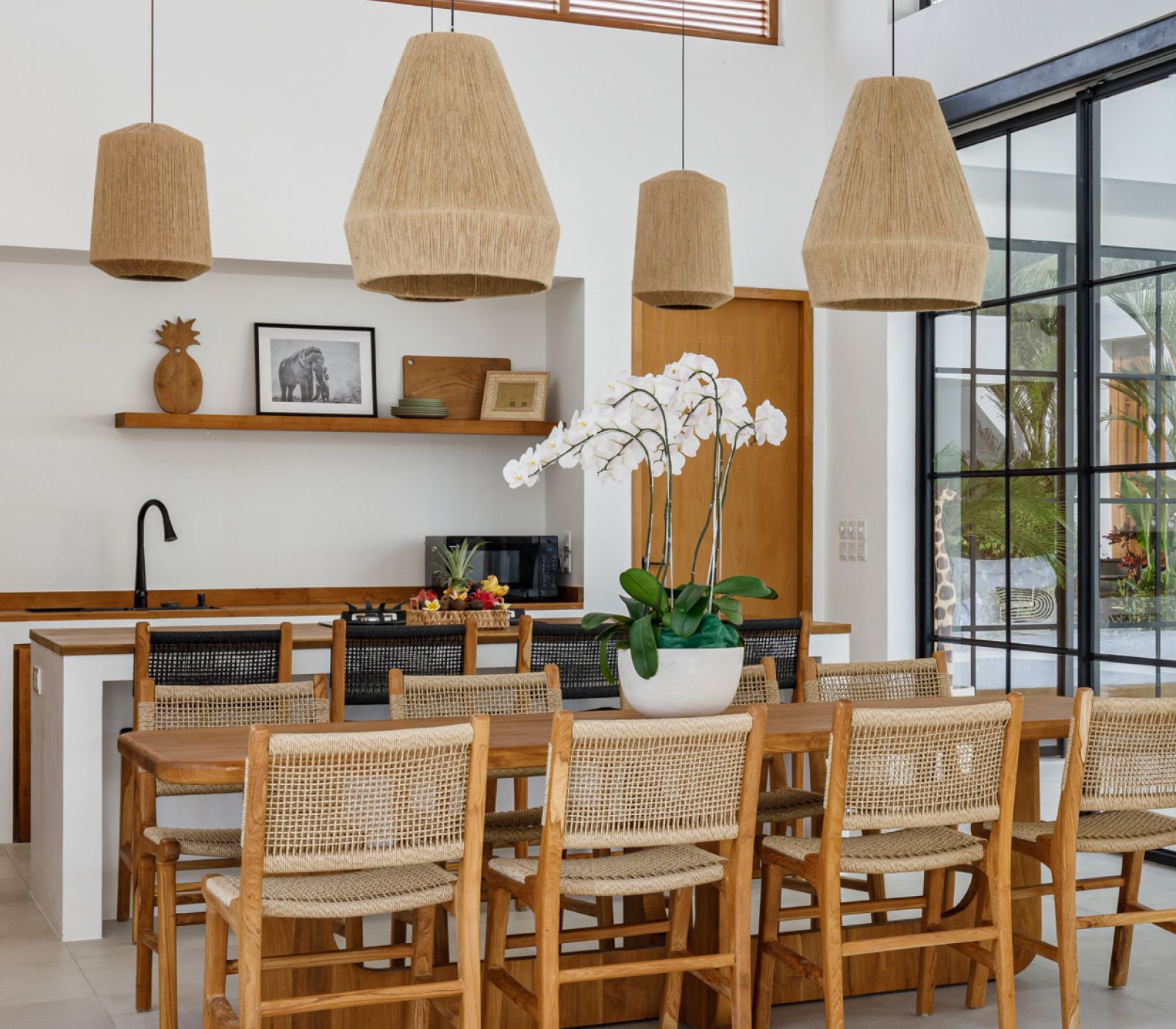 Bright modern dining room with wicker chairs, woven pendant lights, and a kitchen island with orchids