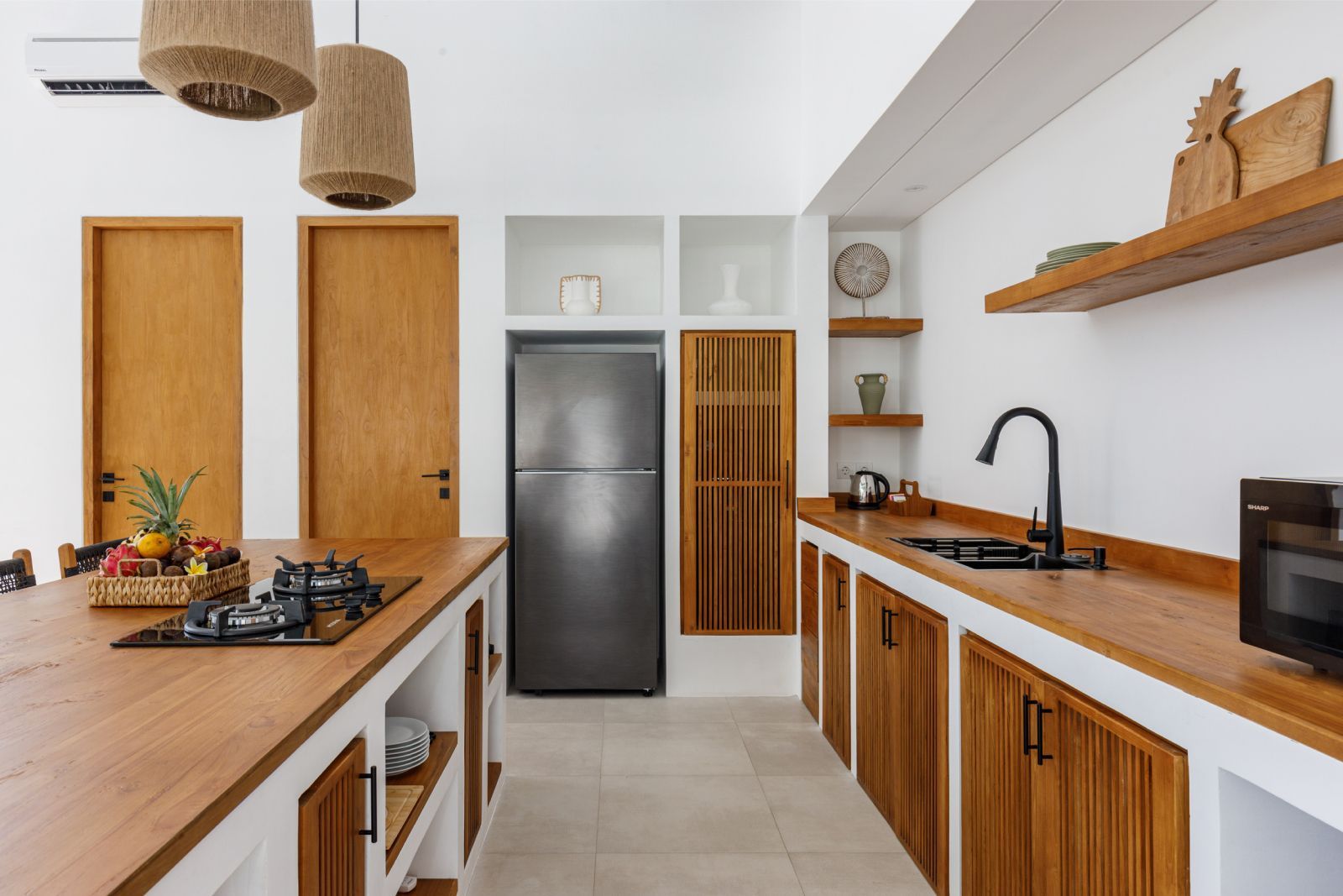 Modern kitchen with wood cabinets, stainless fridge, black countertop, and hanging pendant lights