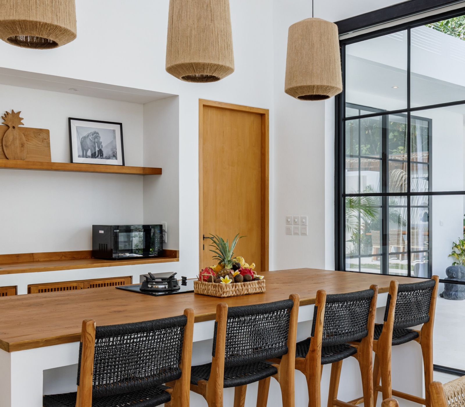 Modern kitchen with wooden island, woven bar stools, pendant lights, and a glass partition.