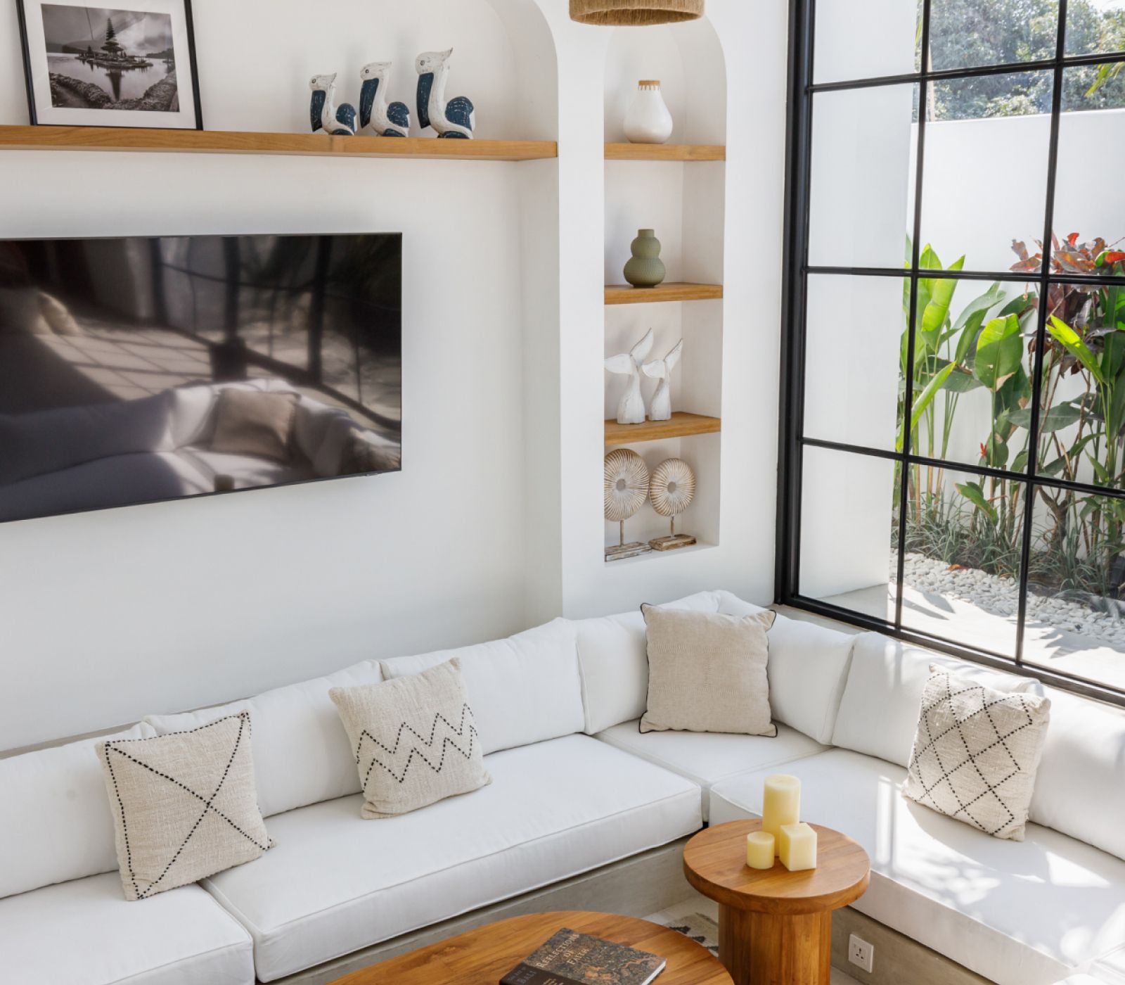Bright living room with white sectional sofa, wall art, shelves, and a large sunlit window.