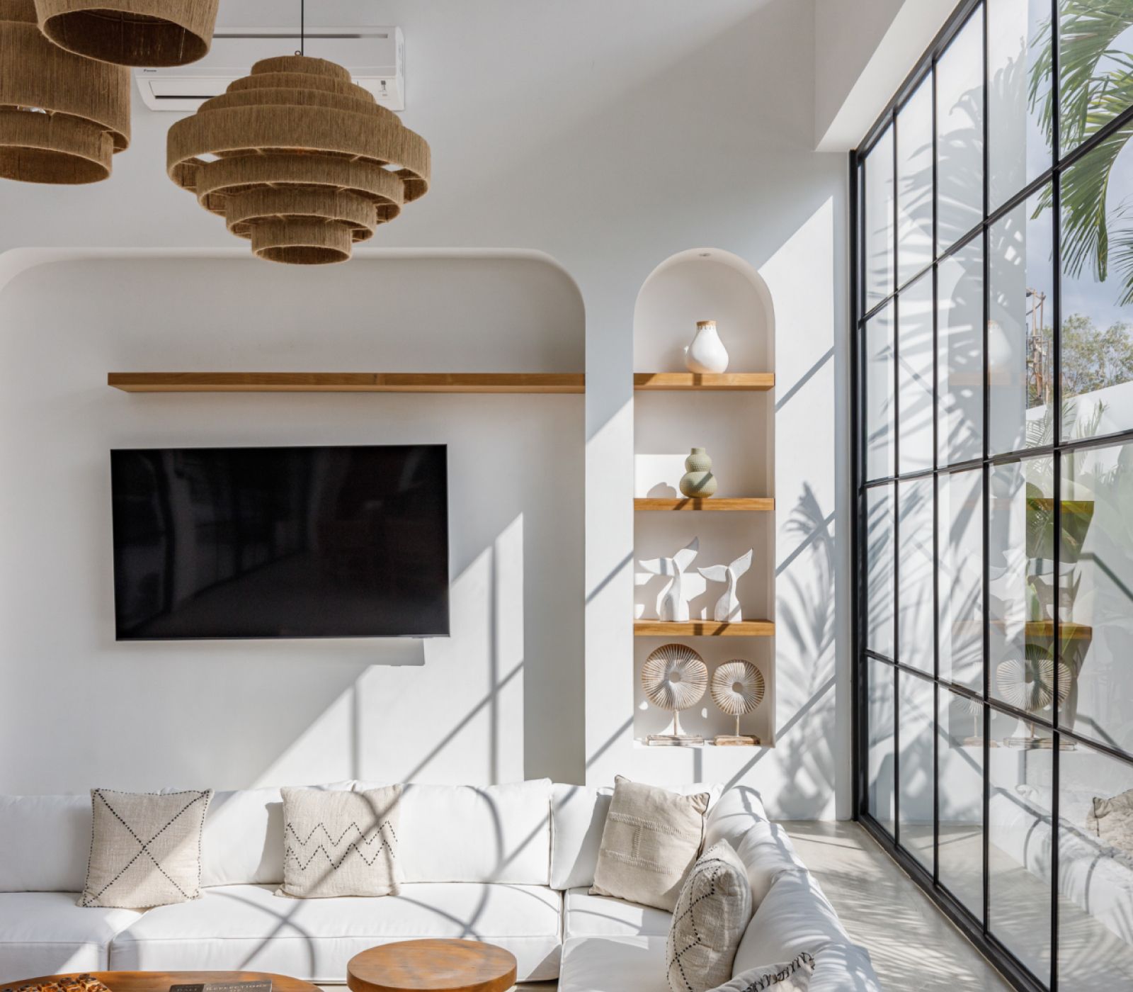 Modern living room with white sofa, wall-mounted TV, arched shelves, and floor-to-ceiling windows