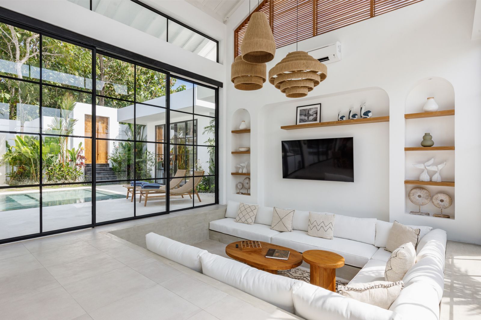 Bright modern living room with white sofa, wall TV, and large glass doors opening to a pool outside