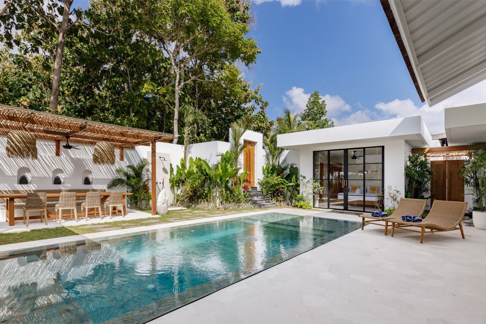 Modern backyard patio with a turquoise pool, lounge chairs, and a white house under a blue sky