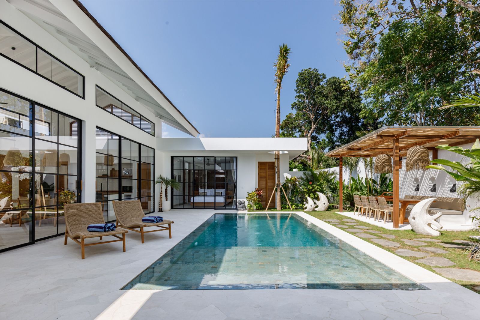 Modern house patio with a long swimming pool, lounge chairs, and a pergola in bright daylight