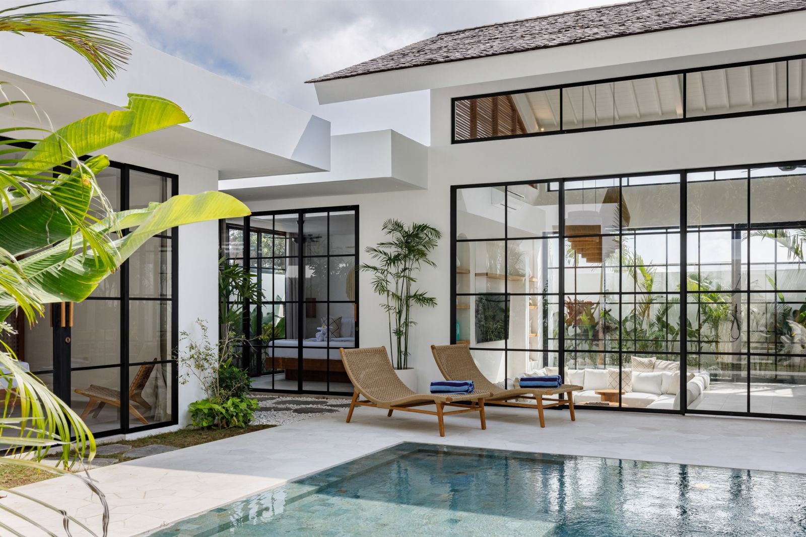 Modern patio with a swimming pool, lounge chairs, and large glass doors on a white house