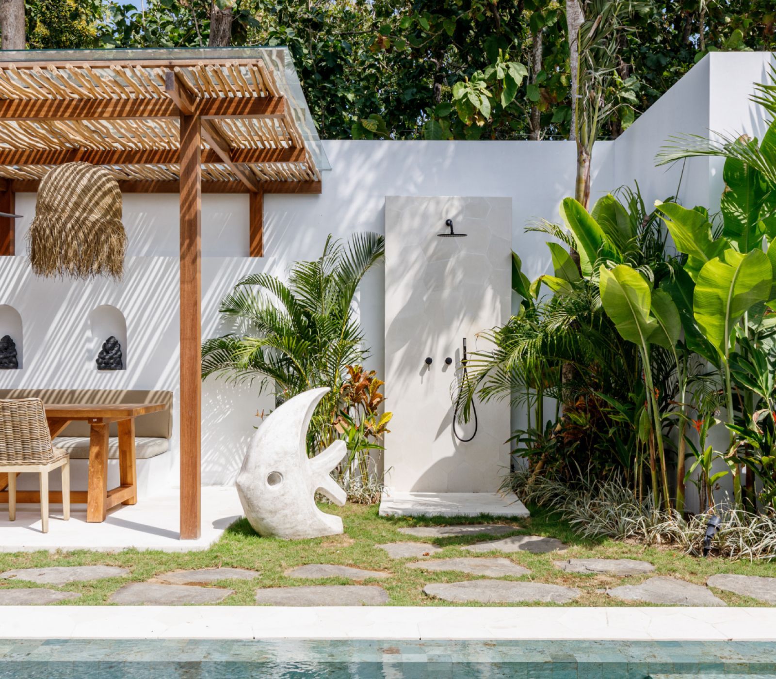Tropical patio with white walls, wooden pergola, hanging chair, and lush green plants.