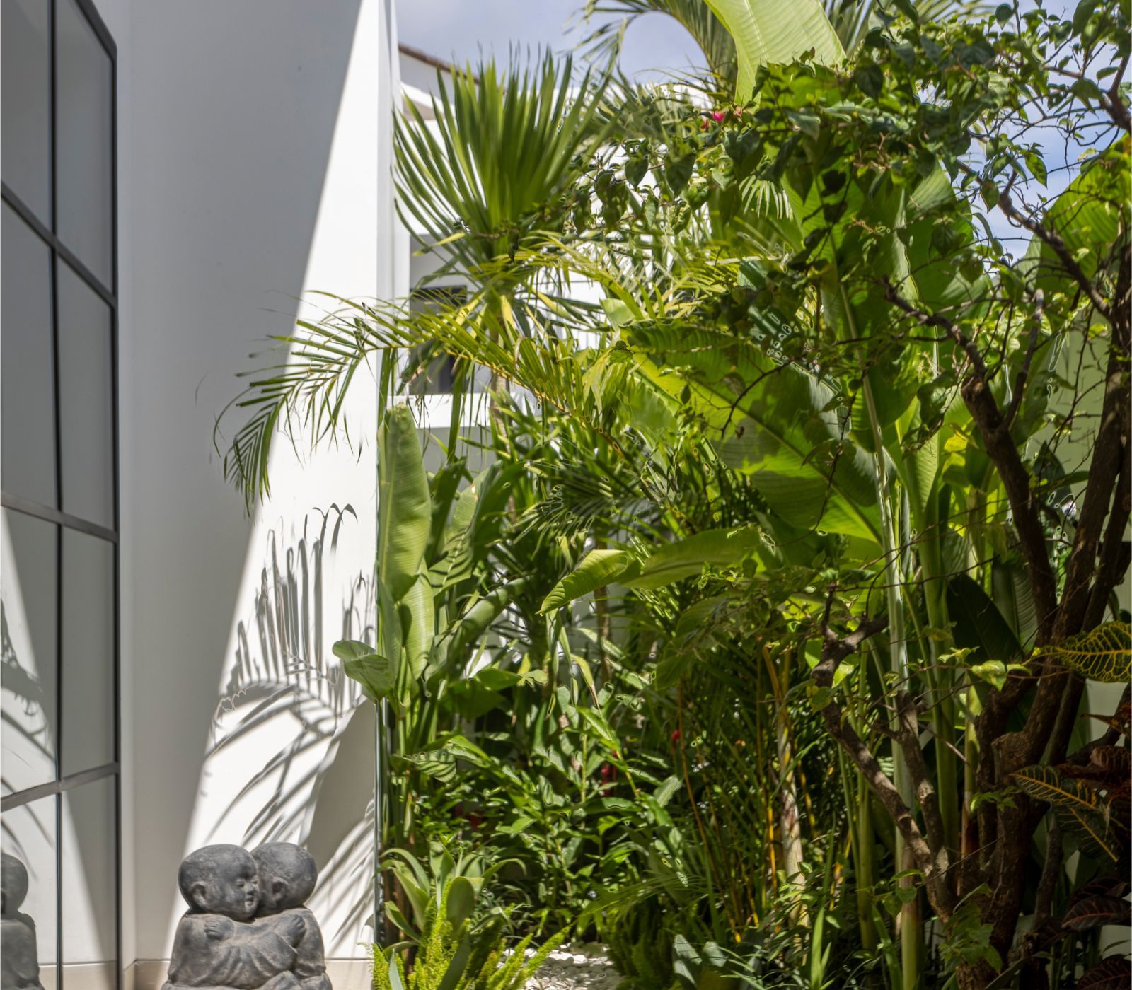 Lush tropical plants beside a modern white wall with a small stone sculpture in the foreground