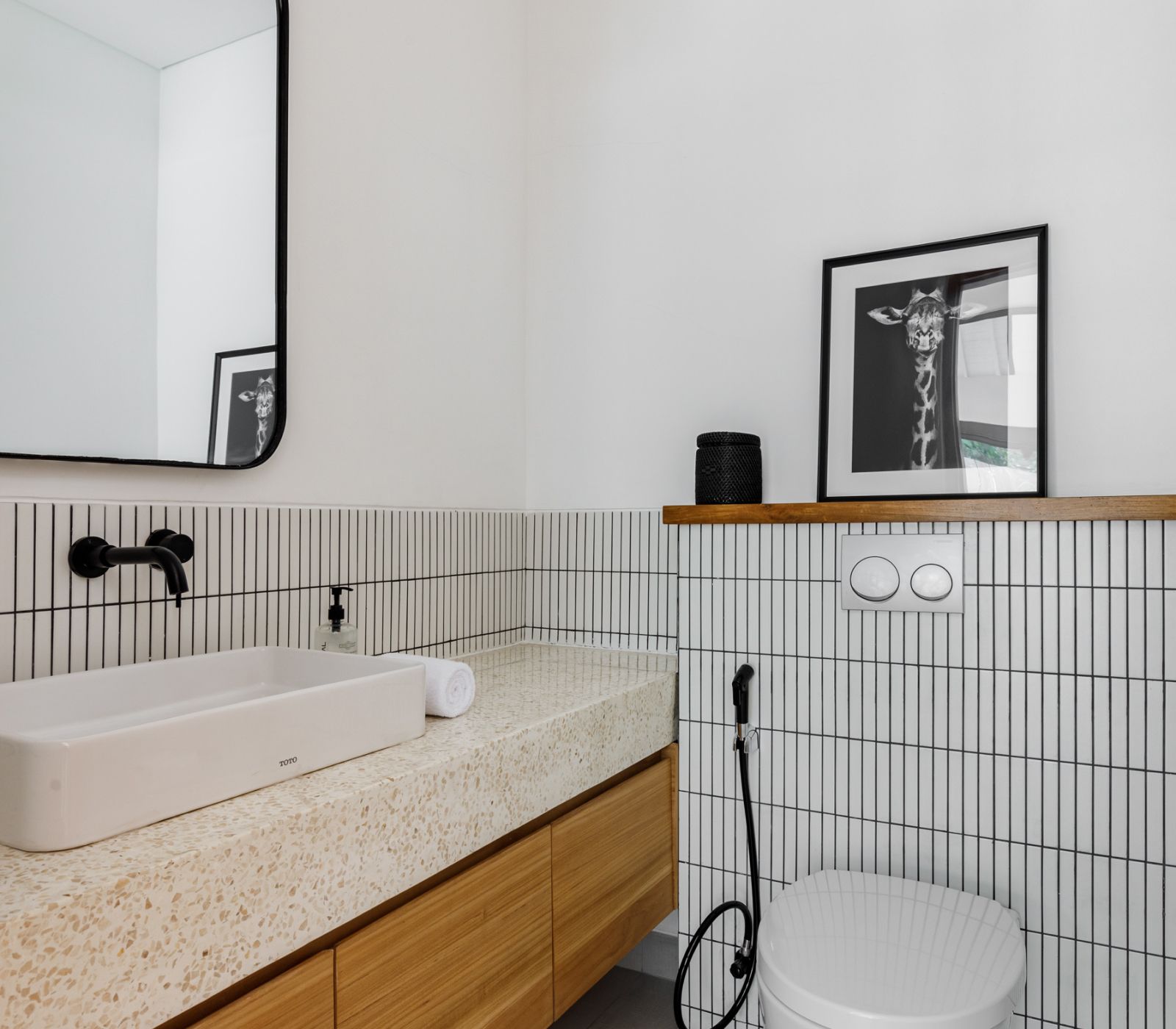 Modern bathroom with terrazzo sink, black fixtures, striped tile, mirror, and toilet under a framed print