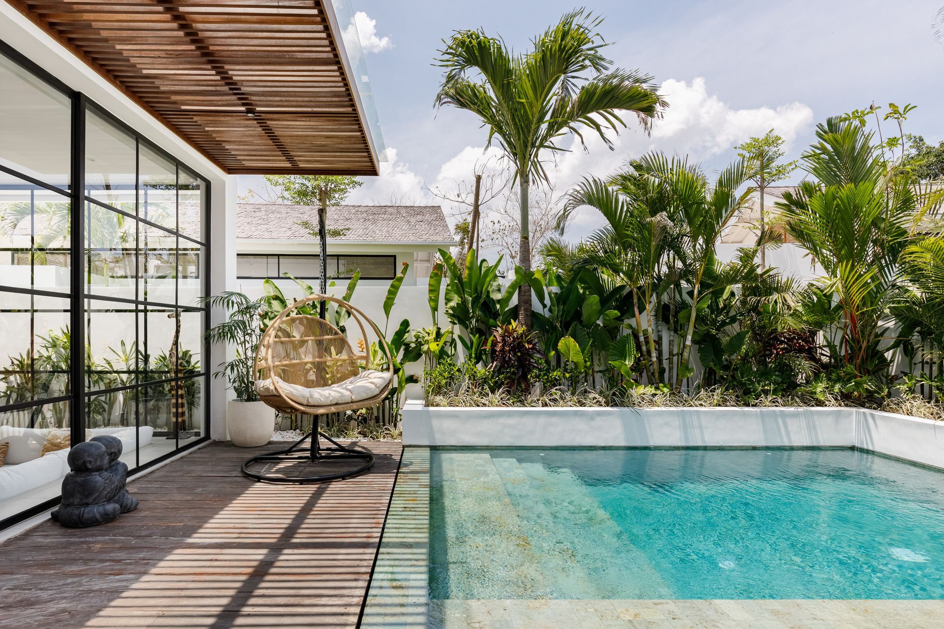 Modern patio with a wicker chair beside a turquoise pool and lush tropical greenery