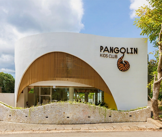 Pangolin Kids Club building with curved white facade and wooden entrance, viewed from the street