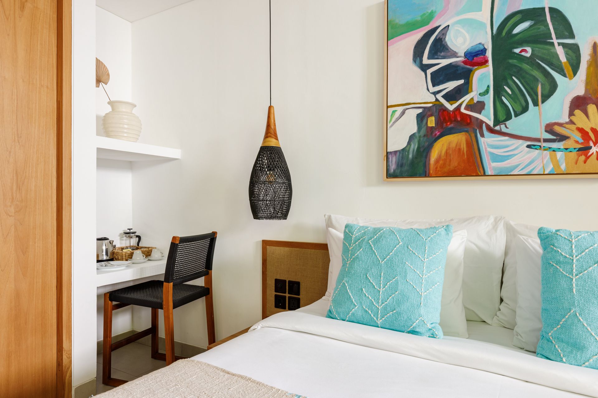 Cozy bedroom with turquoise pillows, white bed, desk nook, and colorful wall art