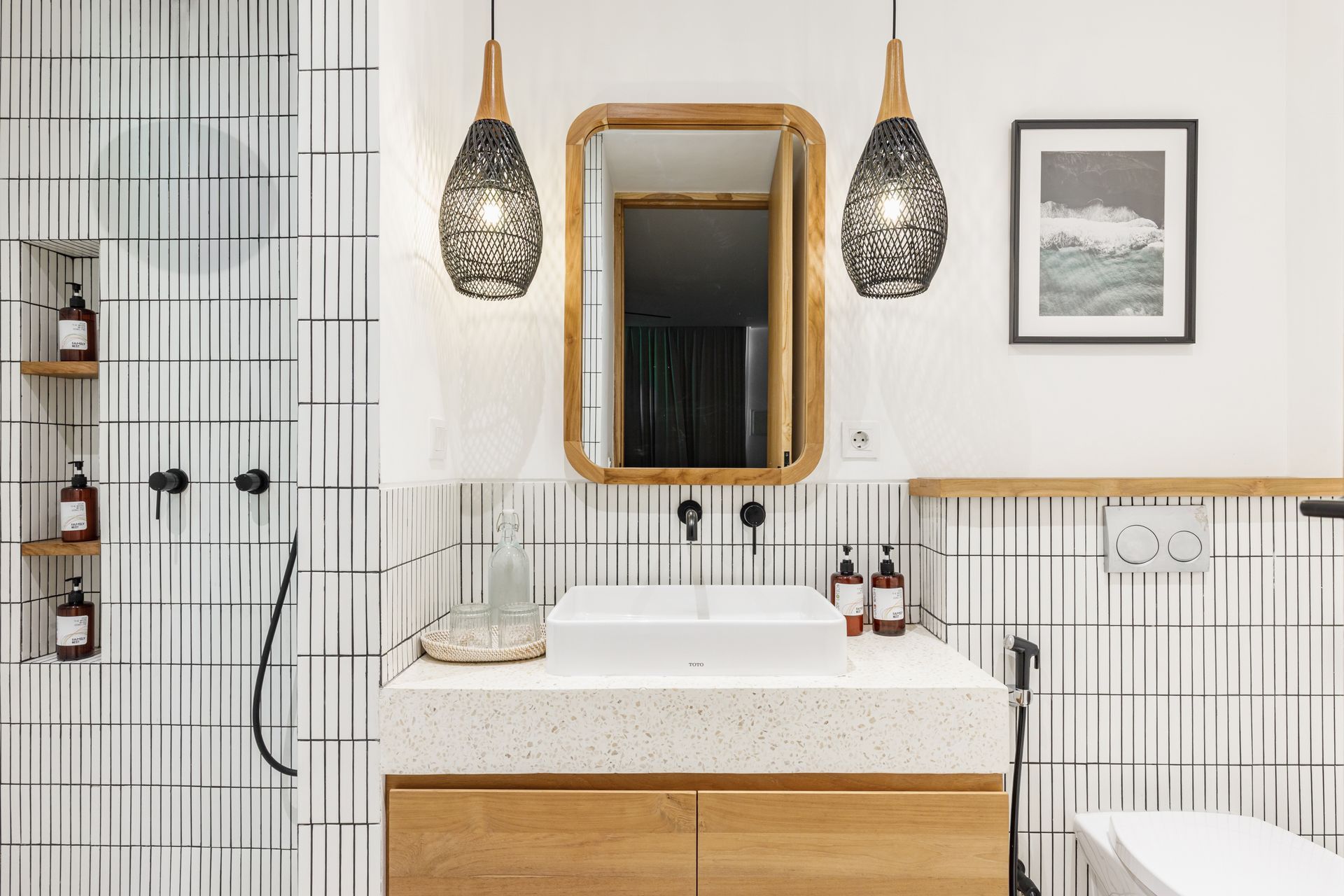 Modern bathroom with white tile walls, wood vanity, round mirror, and woven pendant lights