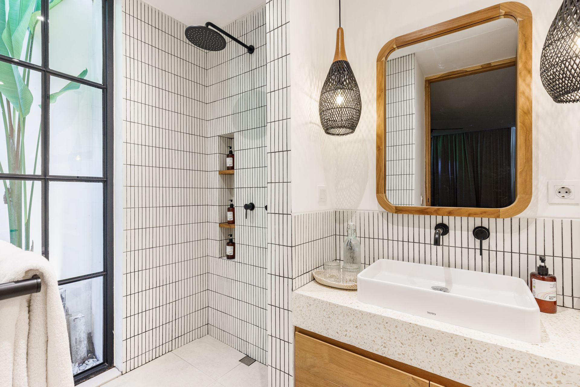 Bright bathroom with white tiled shower, wood-framed mirror, and wood vanity with black fixtures.