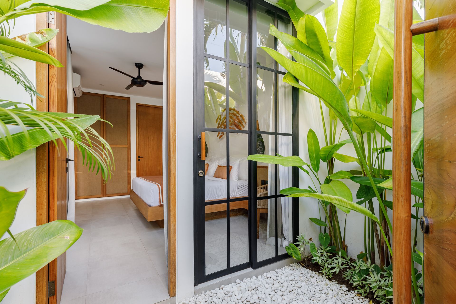 Modern home patio with black-framed glass doors, wooden walls, and lush green plants