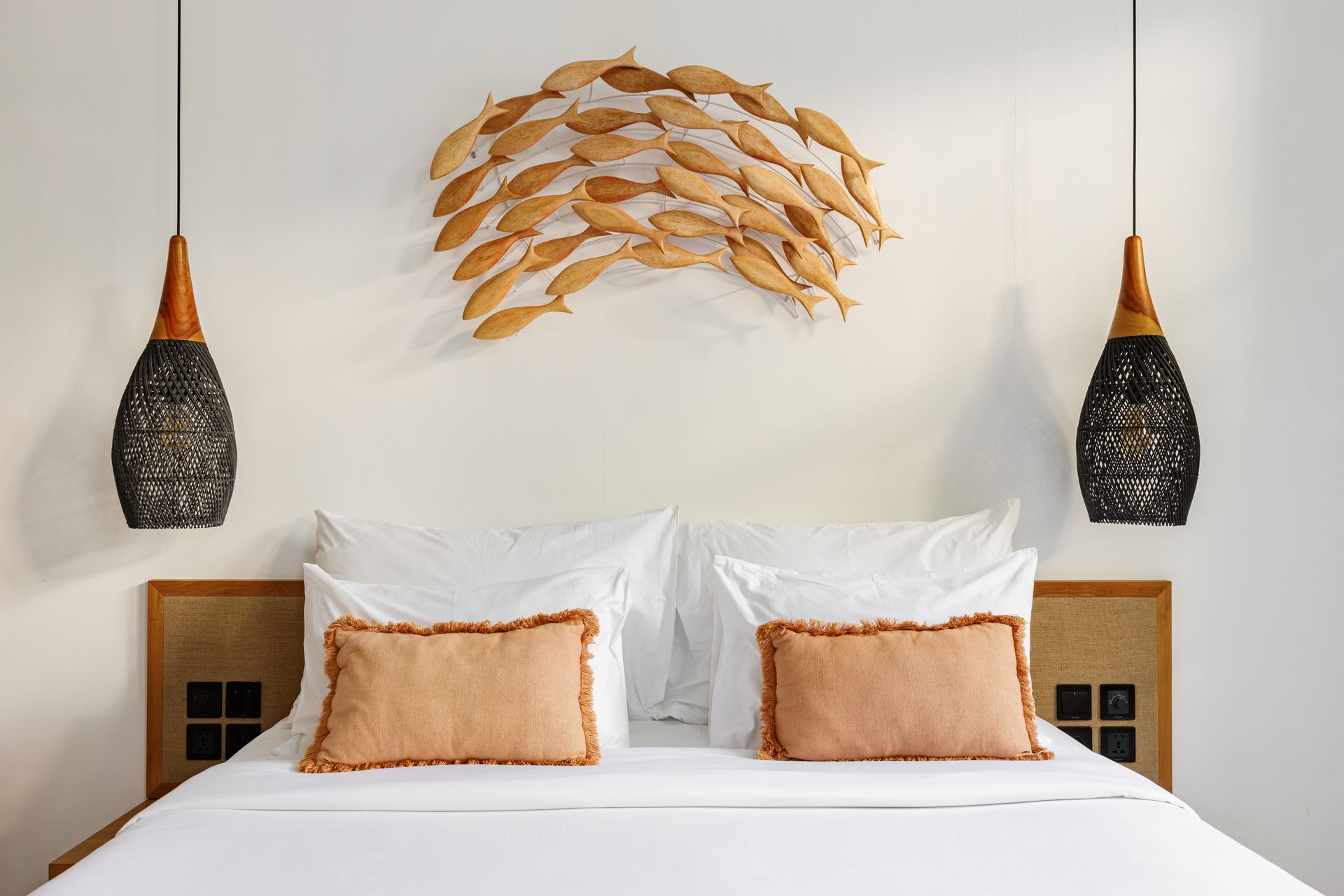 Bed with white linens, tan pillows, and hanging woven pendant lights in a minimalist bedroom.