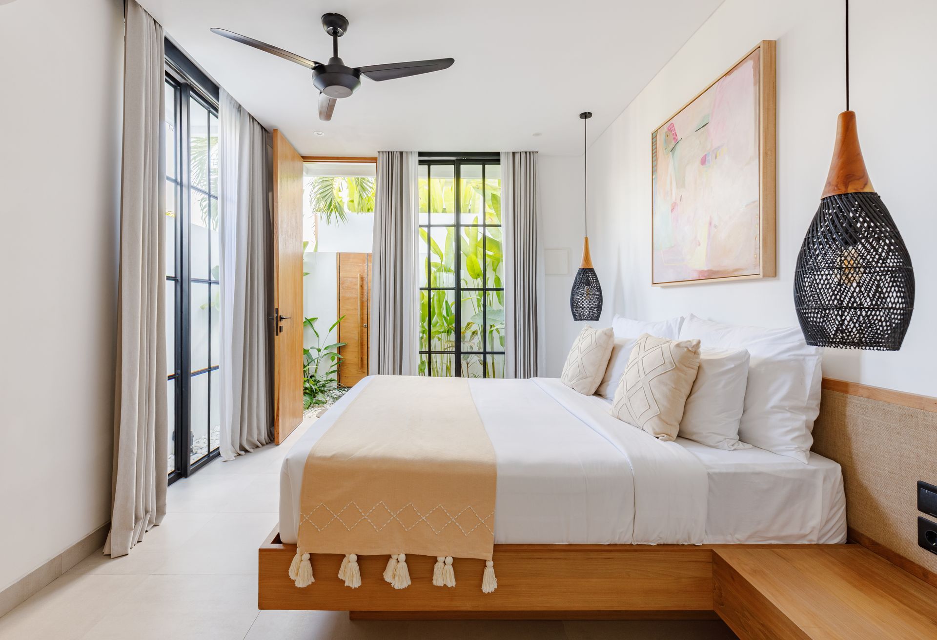 Bright modern bedroom with a large bed, ceiling fan, and sliding glass doors opening to greenery.