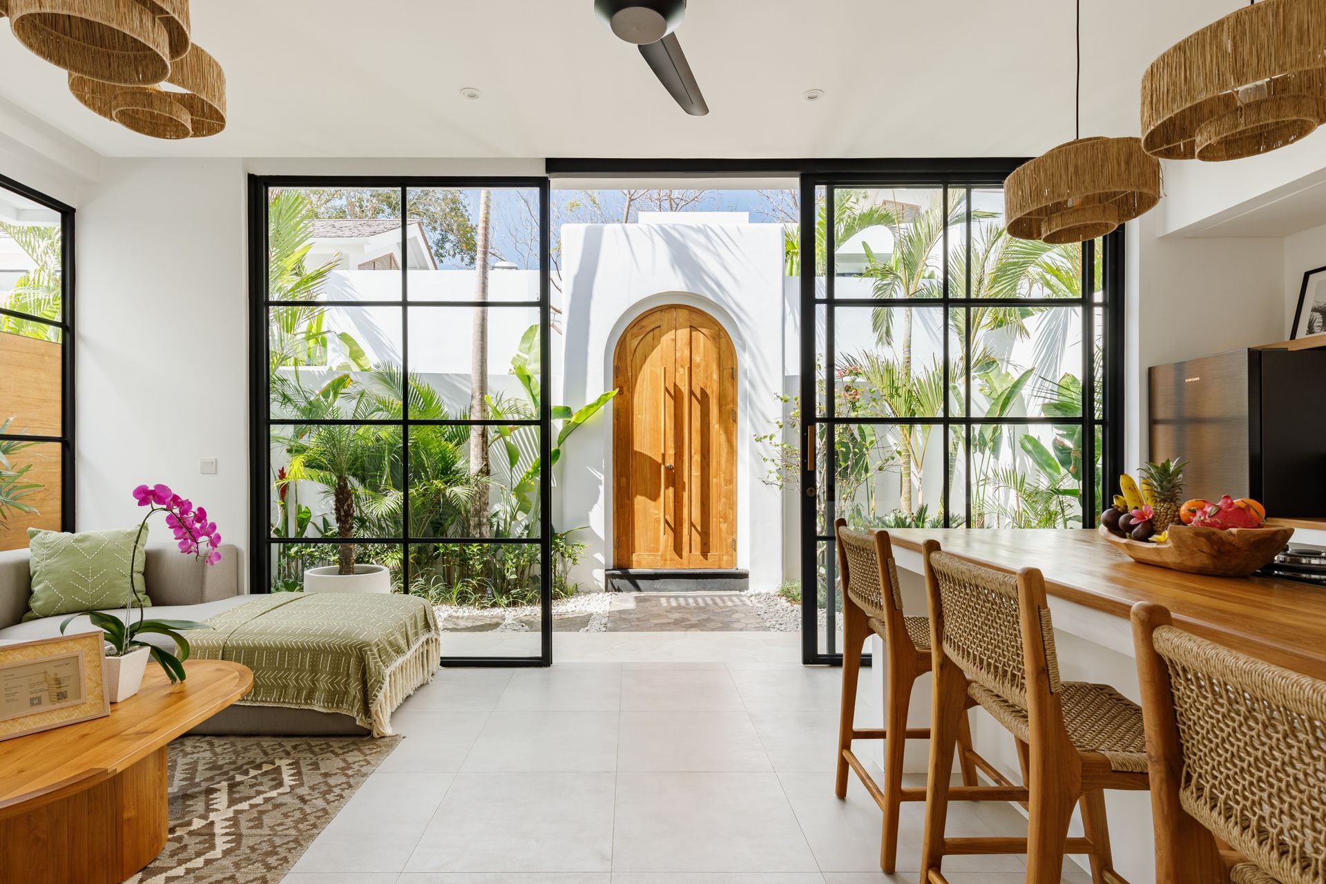 Bright dining room with large glass doors opening to a sunlit courtyard and wooden table set with fruit