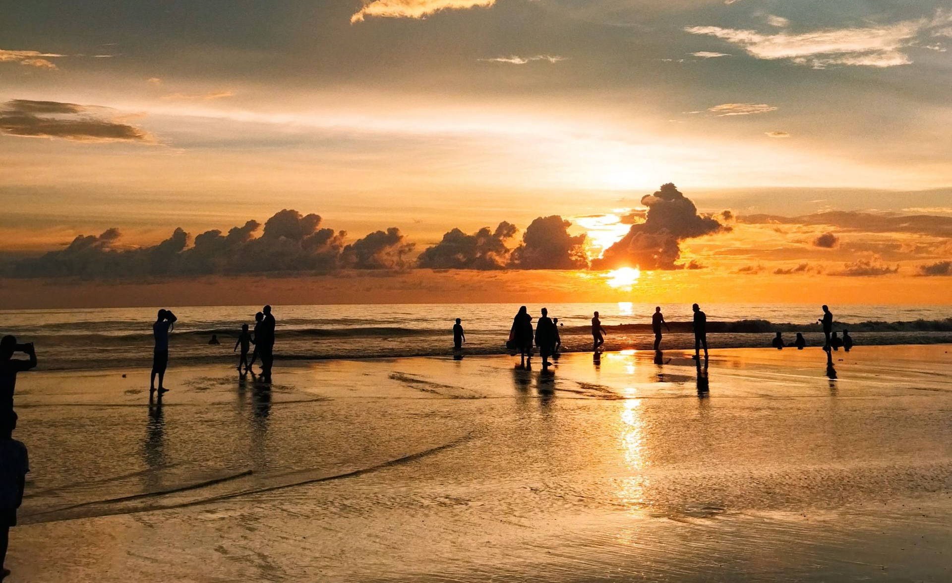 Sunset over wet beach with silhouetted people standing in shallow water