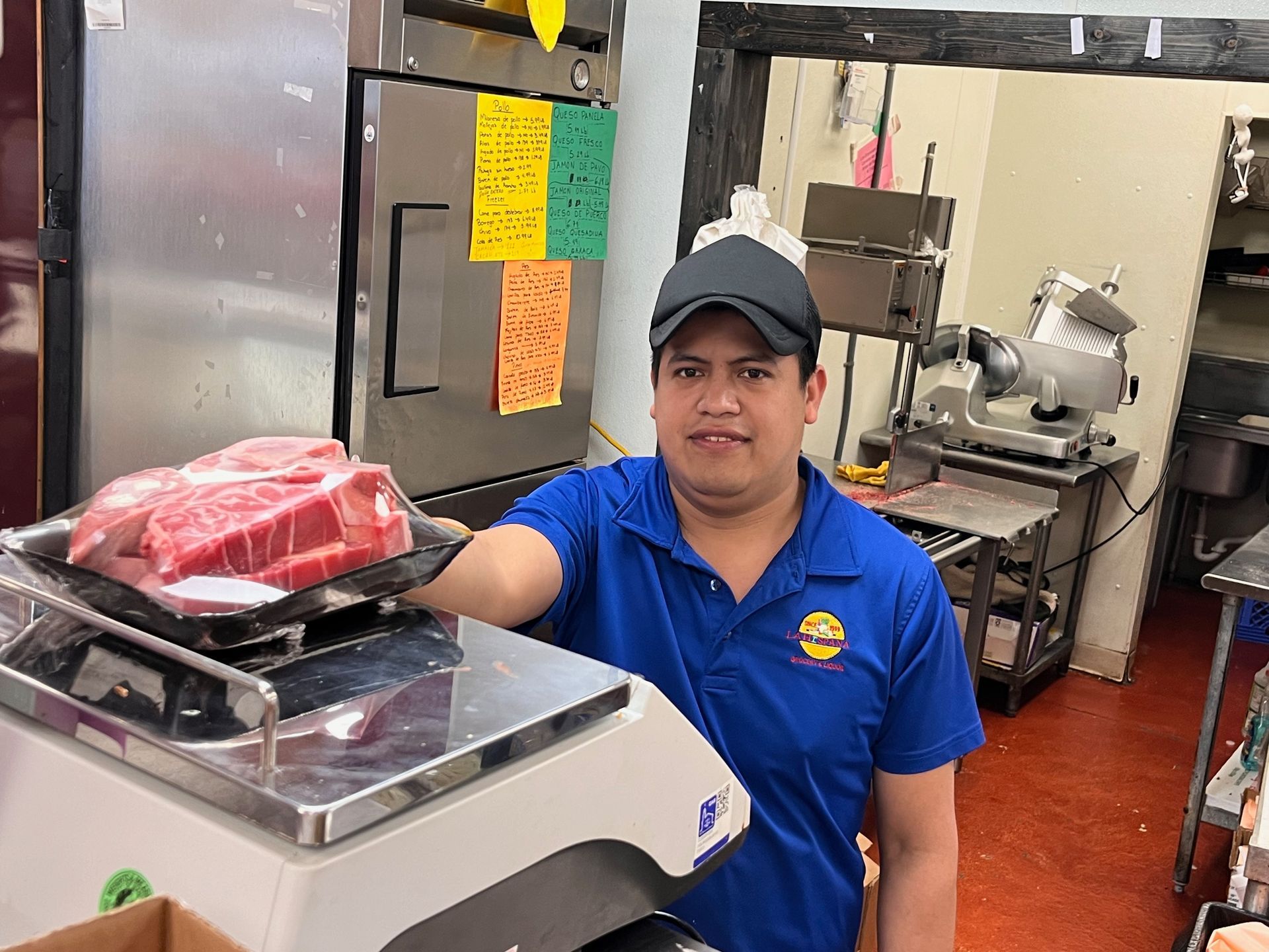 A man in a blue shirt is holding a tray of meat on a scale.