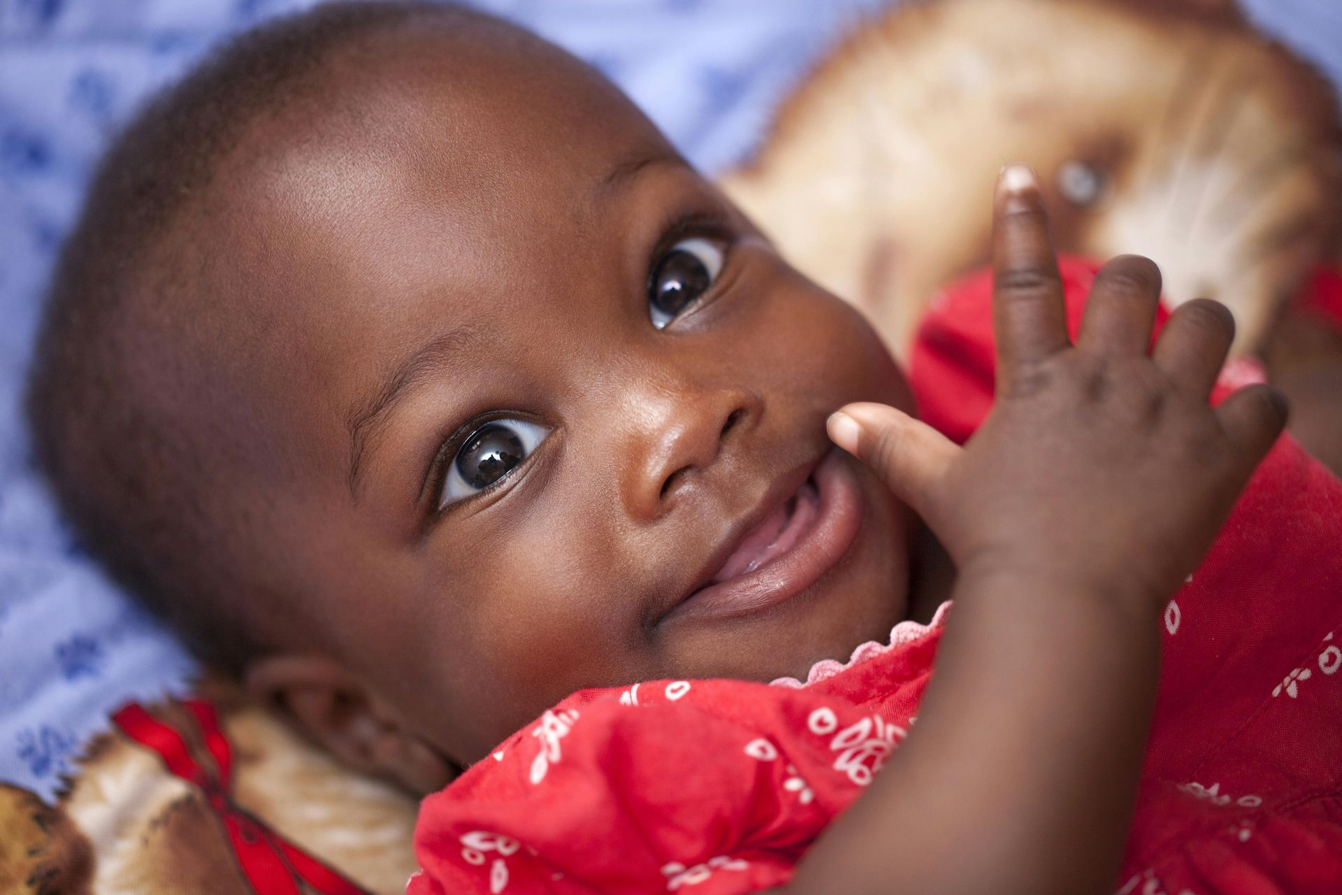 Smiling baby in a red outfit lying down and looking at the camera