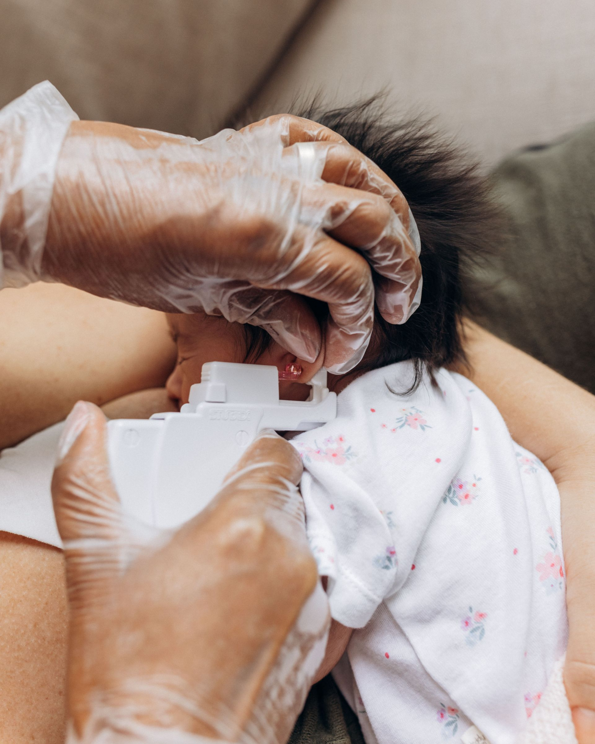 Gloved hands adjusting a white collar on a child in a pink patterned shirt on a couch
