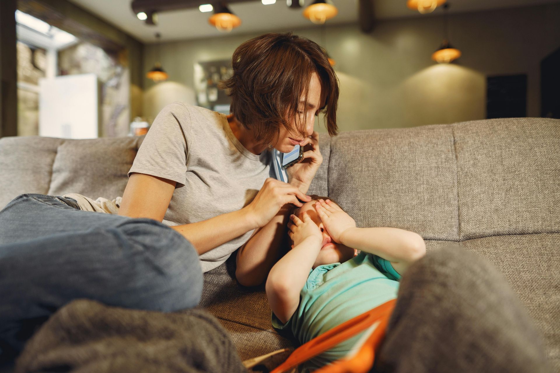 Person lying on a couch while another gently holds their hands in a cozy living room.